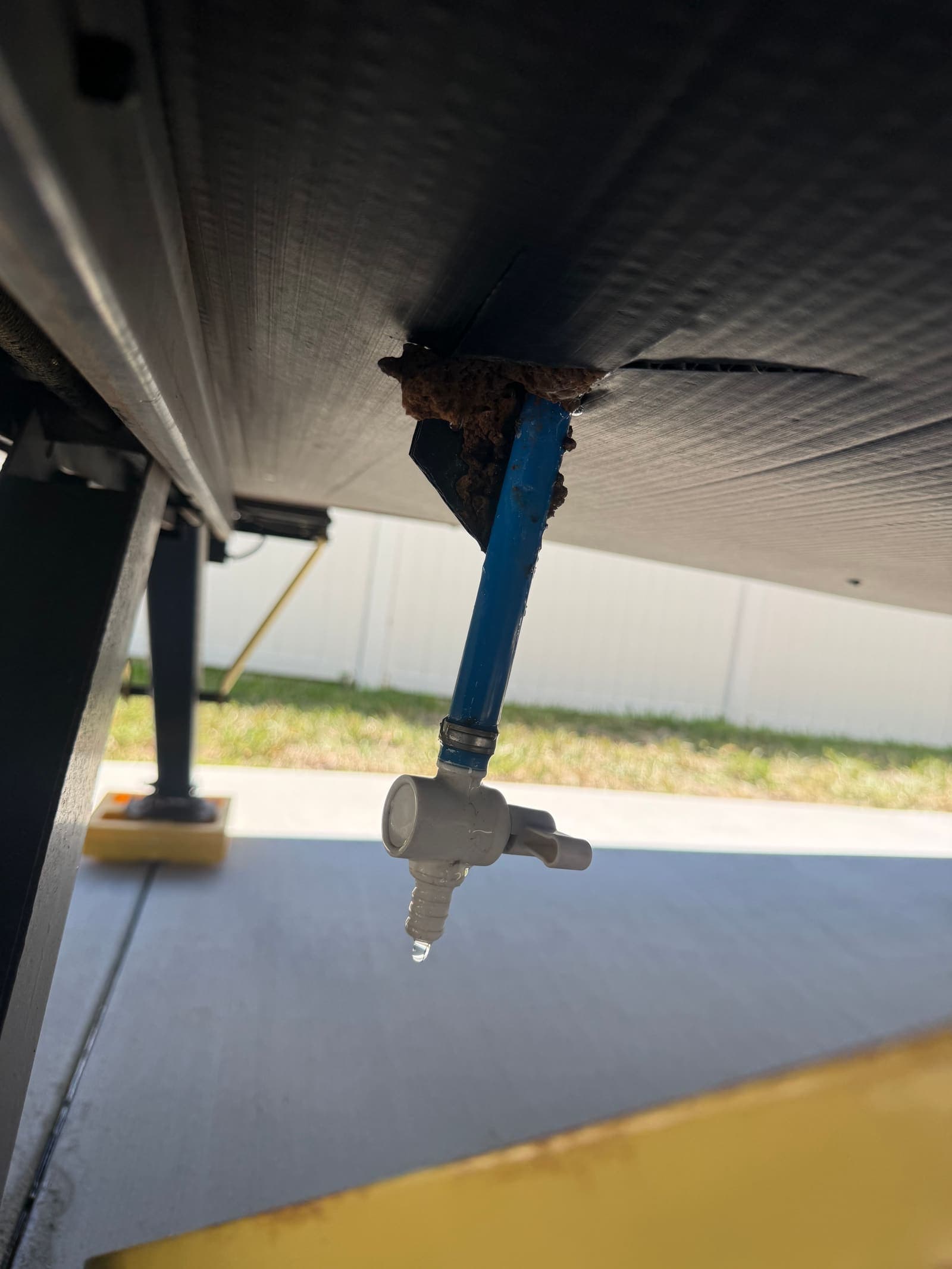 Leaking RV water valve under the chassis with mud dauber nest at the pipe entry
